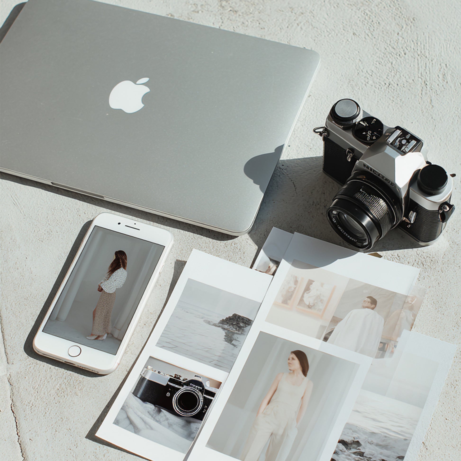 Laptop, smartphone, camera, and photo prints on a light surface. RBF Studio helping founders plan their visual branding.