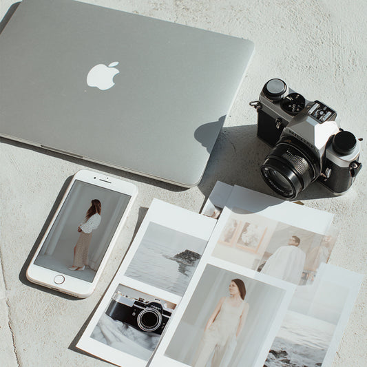 Laptop, smartphone, camera, and photo prints on a light surface. RBF Studio helping founders plan their visual branding.